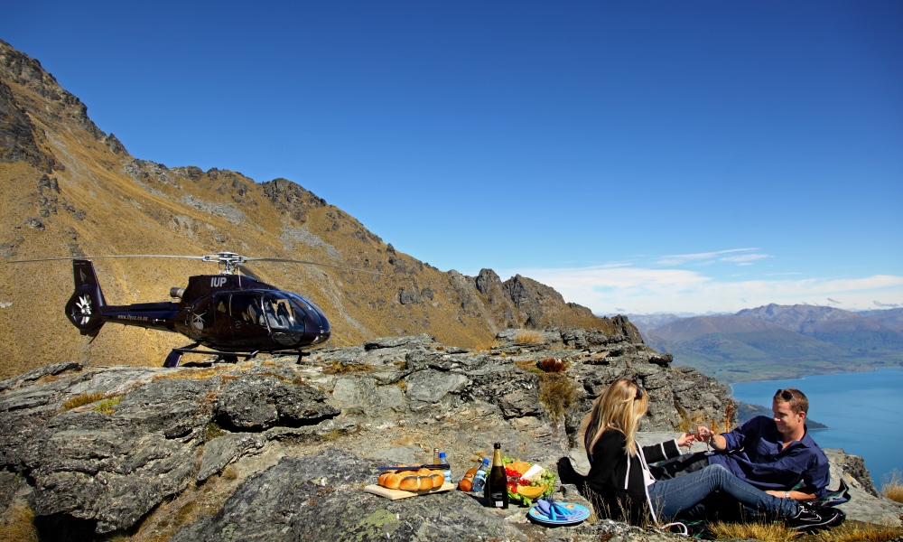 A couple enjoy a romantic picnic on a mountain peak near Queenstown, accessible only by helicopter | Over The Top Helicopters Queenstown