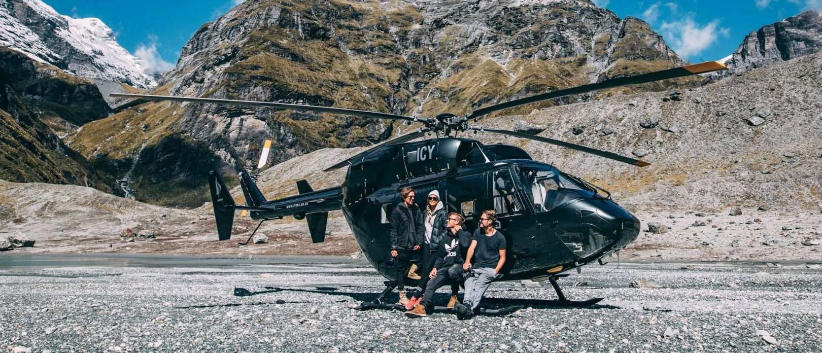 A group of people smiling, perched on the edge of a stationary helicopter